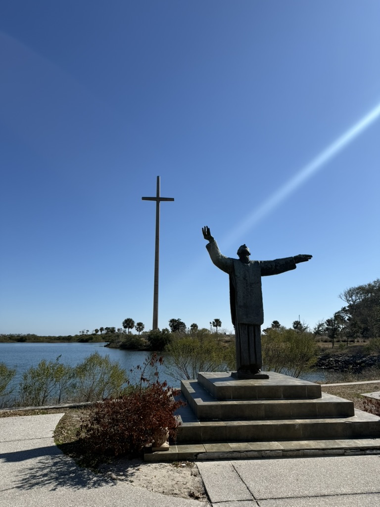 Bronze statue of Father Francisco López with the Great Cross in the background